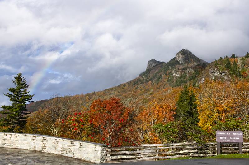 A rainbow forms over Grandfather Mountain’s iconic peaks, as fall color brightens up the foreground at the park’s Half Moon Overlook.